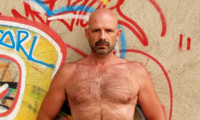 Paco Tantra con su torso peludo apoyado en un muro de ladrillo con grafitis en Barcelona